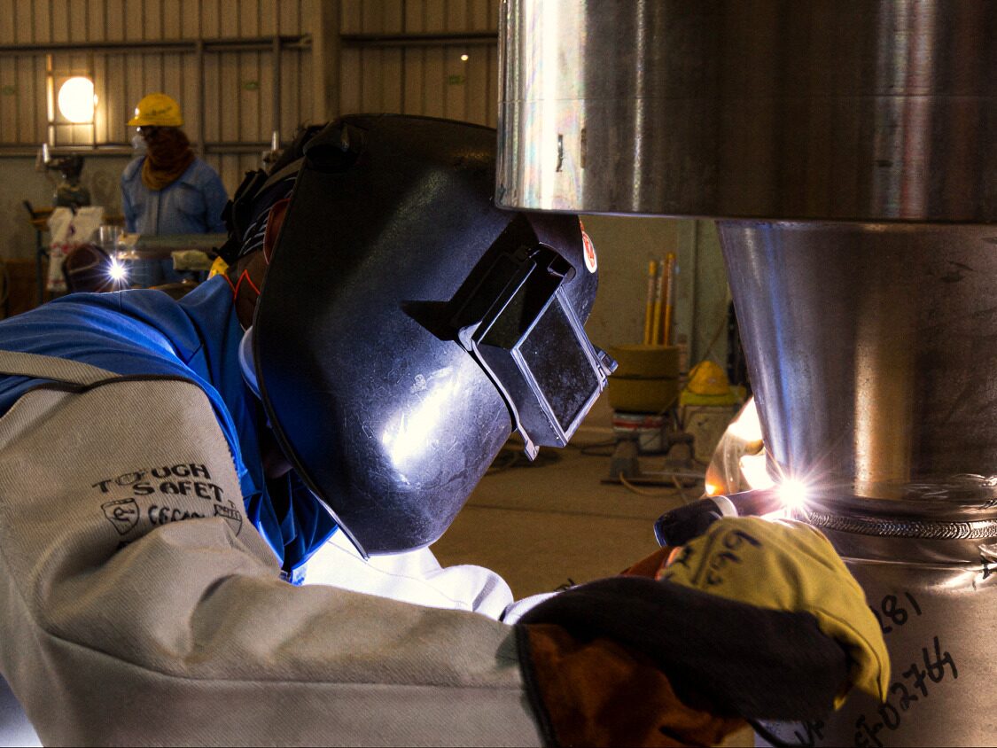 Welder in a protective helmet welding a steel pipe section